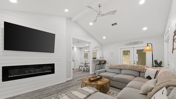 Un salon moderne avec un canapé d’angle, une cheminée, un téléviseur à écran plat et un ventilateur de plafond.
