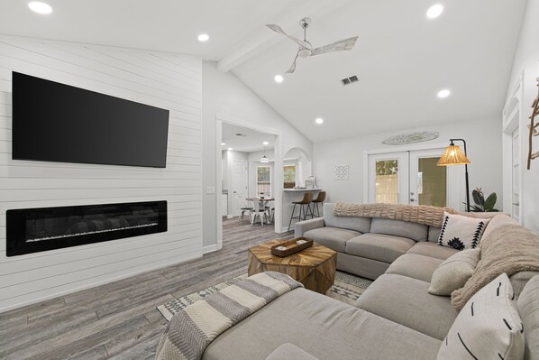A modern living room with a sectional sofa, a fireplace, a flat-screen TV, and a ceiling fan. - Beach Haven 3BR 2bath (Panama City Beach)