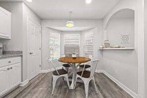 A dining area with a round table, four chairs, a pendant light, and a window with blinds. - Beach Haven 3BR 2bath (Panama City Beach)