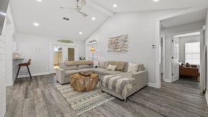 Un salon moderne avec un canapé d’angle, une table basse en bois et un ventilateur de plafond.