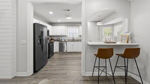Une cuisine moderne avec des meubles blancs, un réfrigérateur noir et un coin bar équipé de deux tabourets.