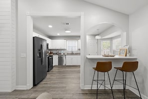 A modern kitchen with white cabinetry, a black refrigerator, and a bar area with two stools. - Beach Haven 3BR 2bath (Panama City Beach)