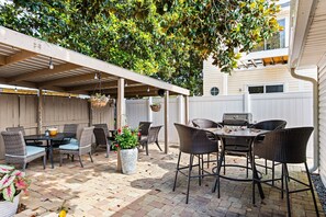 An outdoor patio with wicker furniture, a grill, and hanging plants. - Beach Haven 3BR 2bath (Panama City Beach)