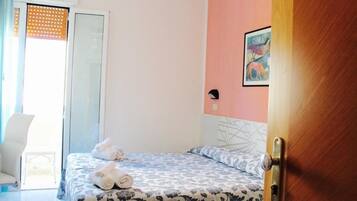 A hotel room with a bed, a chair, a door, and a window with blinds.
