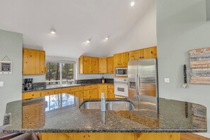 A modern kitchen with wooden cabinets, granite countertops, stainless steel appliances, and a large window.