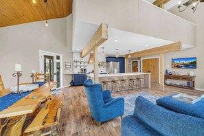 A spacious living area with a wooden dining table, blue upholstered chairs, a bar area, and a kitchen in the background. - GUEST FAV! AC, hot tub, kids playroom, private hot tub, luxury, amazing family home for your Sunriver vacation! Sharc access in 2026! (Sunriver)