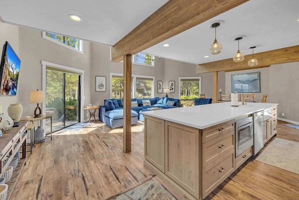 A spacious living area with a large wooden beam ceiling, a central island with a sink, and a seating area with a blue sofa.