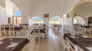 Un restaurant avec des tables dressées pour le service, de grandes fenêtres en arc et une vue sur le paysage.