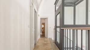 Un couloir au sol en pierre mène à une salle de bain équipée de toilettes et d’un lavabo.