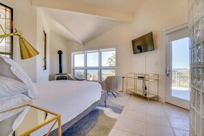A bedroom with a large bed, a desk, a chair, a television, and a window with a view.