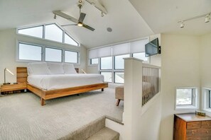 Un dormitorio moderno con una cama grande, ventilador de techo y varias ventanas.