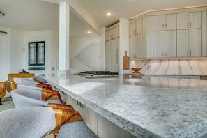 Una cocina moderna con encimeras de mármol, sillas de madera y armarios de tonos claros.