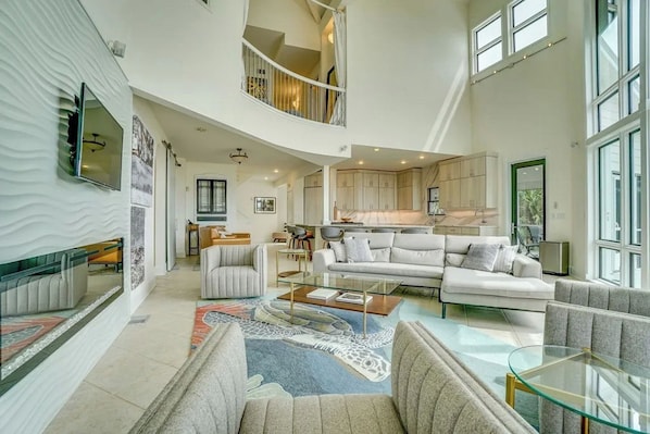 A spacious living area with a high ceiling, a kitchen with modern cabinetry, and a dining area with a glass coffee table.
