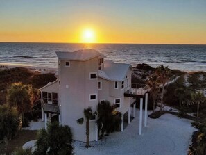 A coastal property with a multi-level structure, a balcony, and a view of the ocean at sunset.