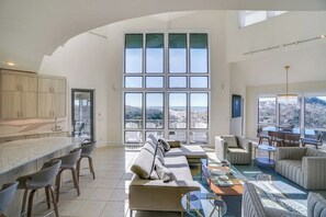 Amplia sala de estar con un ventanal grande, una cocina con encimera de mármol y una zona de estar con sofá y sillones.