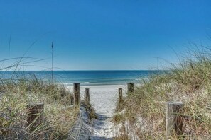 A sandy beach path leading to the ocean, surrounded by grass and wooden posts.