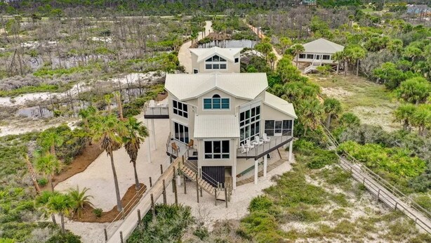 A large, multi-story beachfront property with a prominent central building featuring large windows and a balcony.