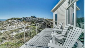 A beachfront property with a wooden deck, white chairs, and a view of the ocean.