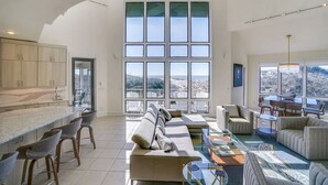 A spacious living area with a large window offering a view of the outdoors. There is a kitchen area with modern cabinetry and a bar counter.