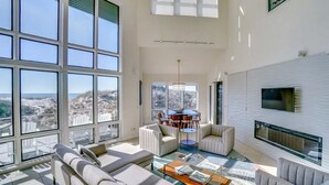 A spacious living room with large windows, a fireplace, and a dining area with a view of the beach.