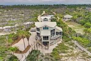A coastal property with a large house featuring multiple levels, a covered deck, and a staircase leading to the main entrance.