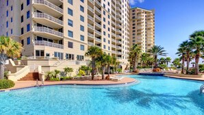 Un hôtel doté d’une piscine, de palmiers et d’un immeuble à plusieurs étages avec des balcons.