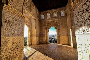 Un intérieur agrémenté d’arcs décoratifs et de sculptures détaillées, un sol en pierre et une vue dégagée sur l’extérieur, visible à travers une arche.