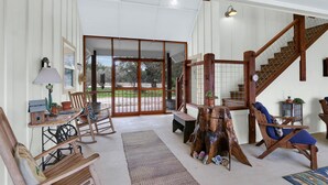 A spacious living area with a wooden staircase, a rocking chair, and a view of the outdoors. - Casa Robles- Mockingbird I Couples, stargazing (Wimberley)