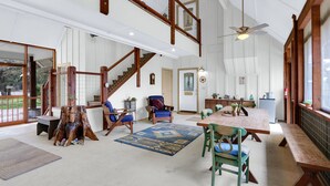 A spacious living area with a high ceiling, wooden staircase, and a dining table with chairs. - Casa Robles- Bluebonnet I Firepit, couples (Wimberley)