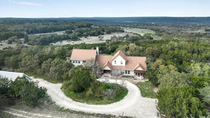 A two-story house with a red roof, surrounded by dense trees and a clear sky. - Casa Robles- Bluebonnet I Firepit, couples (Wimberley)