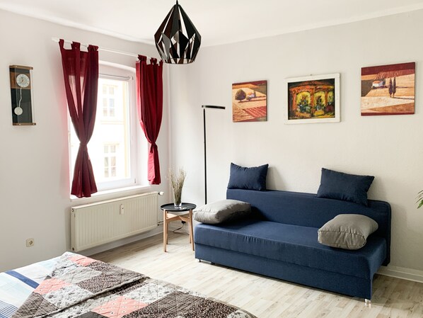 A modern living room with a blue sofa, red curtains, a floor lamp, and three paintings on the wall.