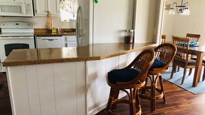 Uma cozinha com ilha de madeira, armários brancos e uma área de refeições com cadeiras de vime.