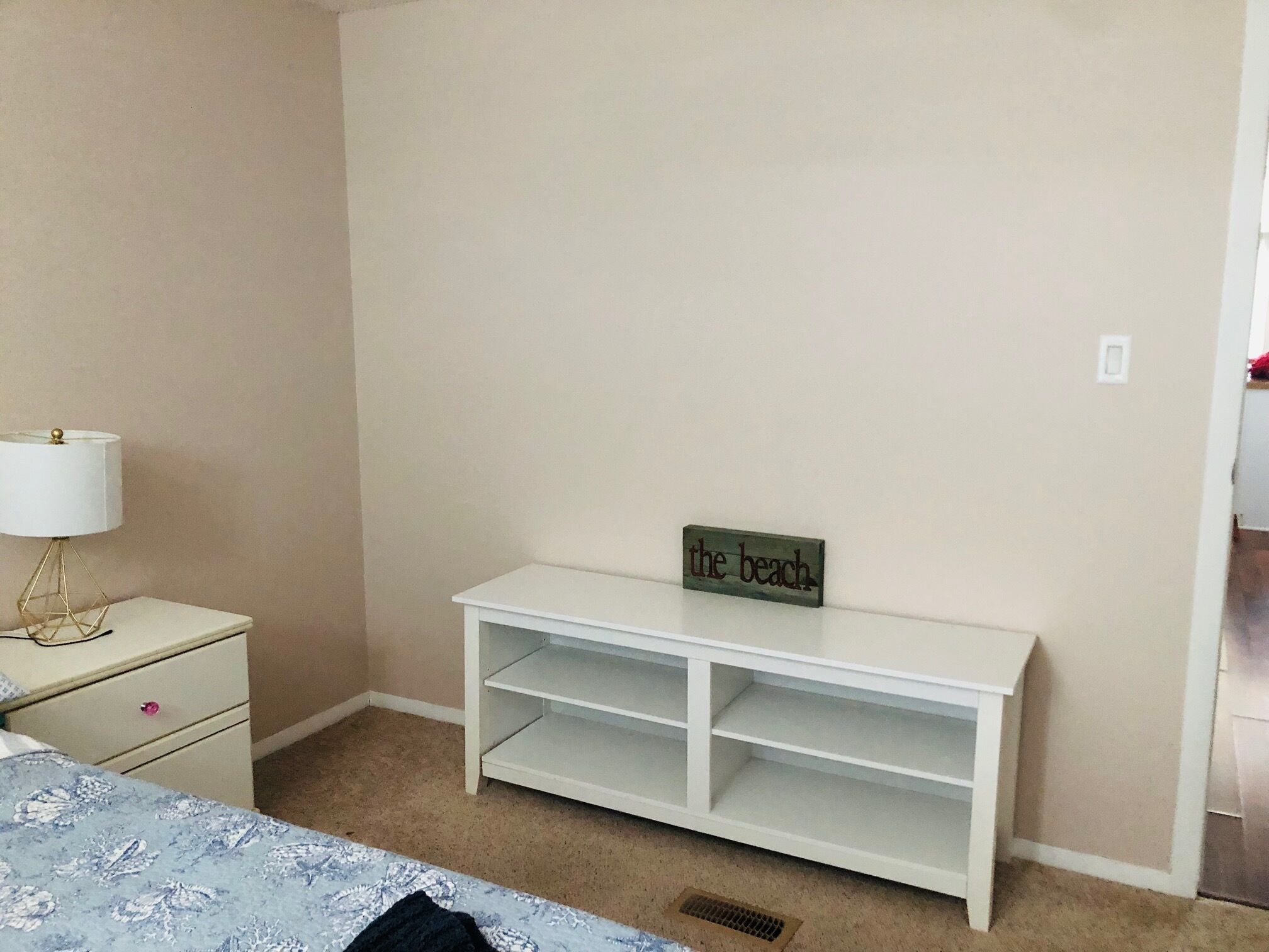 Et soveværelse med en seng, et natbord, en lampe og en hvid kommode.