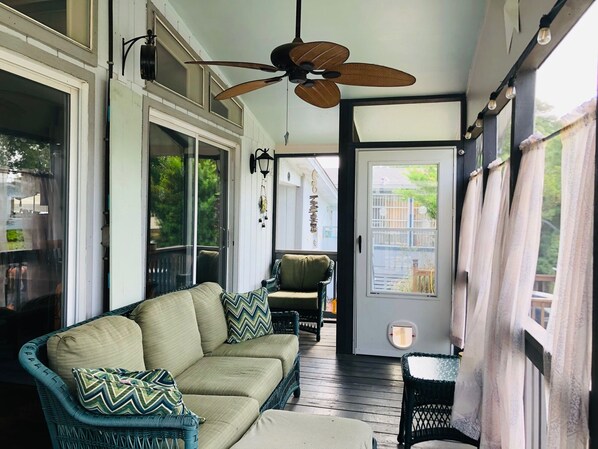 A covered porch with a sofa, chairs, and a ceiling fan.
