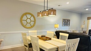 A dining area with a white table and chairs, a chandelier, and a large wall clock.