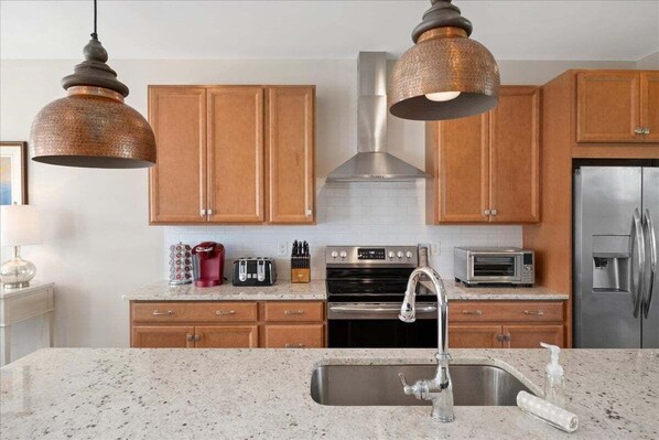Una cocina con armarios de madera, electrodomésticos de acero inoxidable, encimeras de granito e iluminación colgante.
