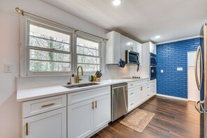 A modern kitchen with white cabinetry, stainless steel appliances, and a blue brick accent wall.