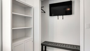 Ein Zimmer mit einem weißen Kleiderschrank, einer Bank und einem Wand-Fernseher.