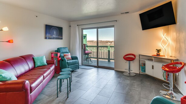 Ein modernes Wohnzimmer mit einem roten Ledersofa, smaragdgrünen Sesseln und einer Glastür, die auf einen Balkon führt.