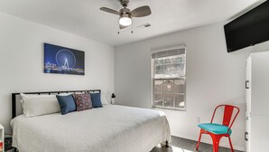 Ein Schlafzimmer mit einem Bett, einem Deckenventilator, einem Fenster, einem roten Sessel und einem an der Wand befestigten Fernseher.