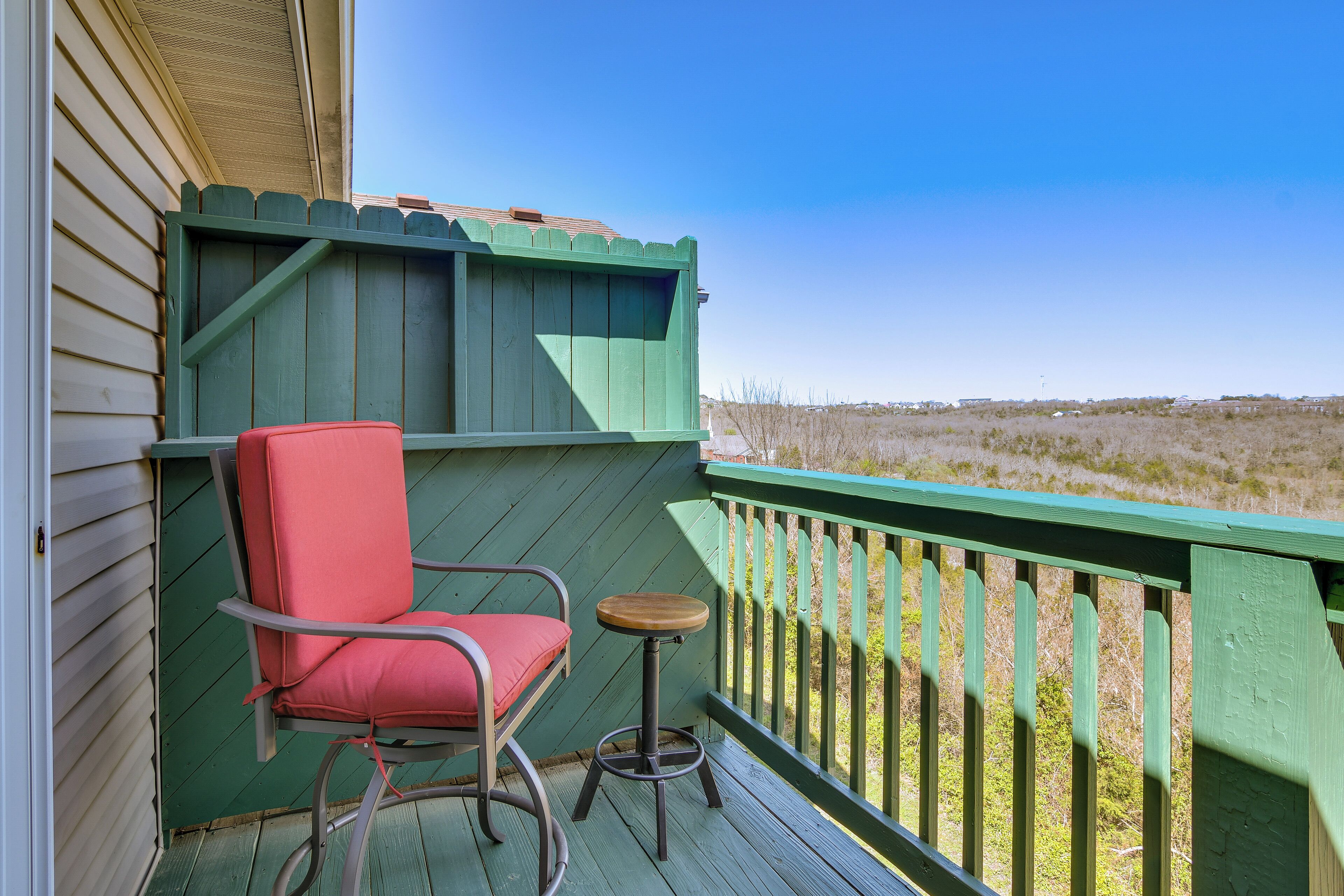 Un balcon avec une rambarde verte, une chaise rouge et une petite table ronde.