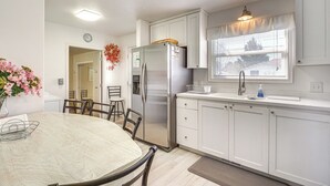 A modern kitchen with white cabinets, a stainless steel refrigerator, a dining table with chairs, and a window with blinds. - Charming Orem Home w/ Yard - Near BYU & Uvu! (Orem)