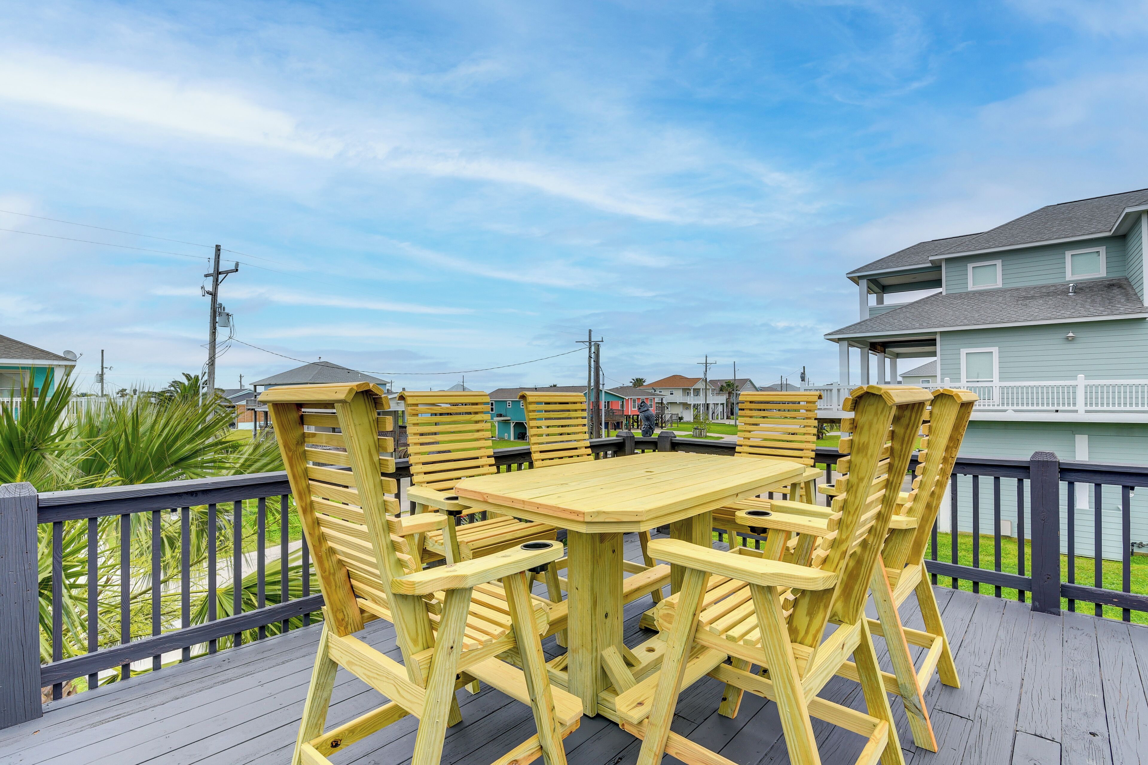 A wooden deck with a table and chairs, surrounded by a railing, overlooking a residential area.