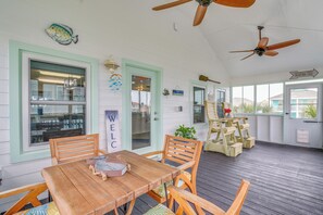 A covered porch with a wooden table and chairs, a ceiling fan, and a view of the house in the background. - Retreat w/ Hot Tub & Fenced Yard: Walk to Beach (Port Bolivar)