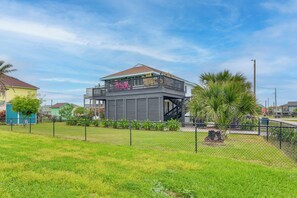 A two-story building with a balcony, surrounded by a chain-link fence and greenery. - Retreat w/ Hot Tub & Fenced Yard: Walk to Beach (Port Bolivar)