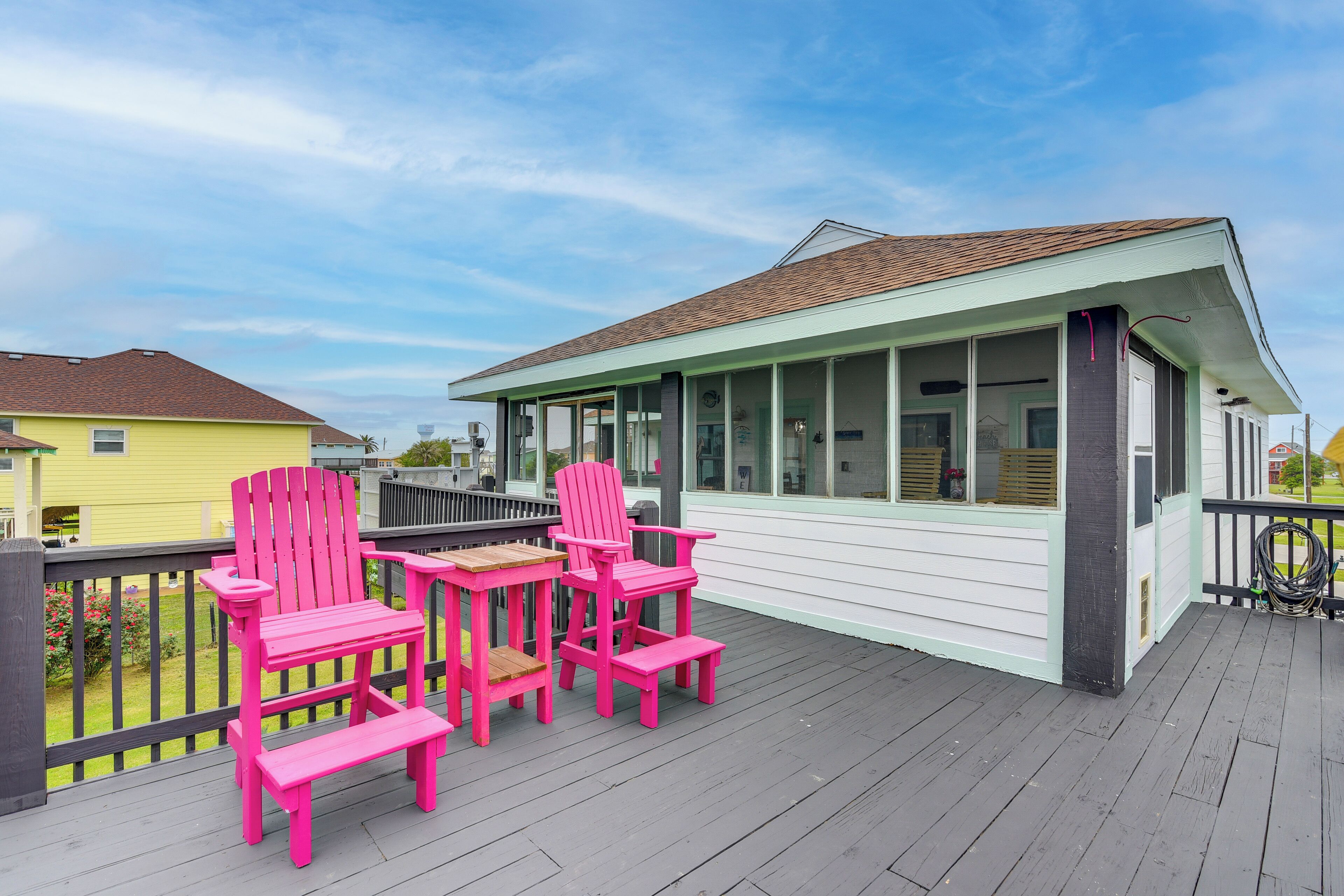 A covered deck with a white building, a yellow building in the background, and pink chairs.