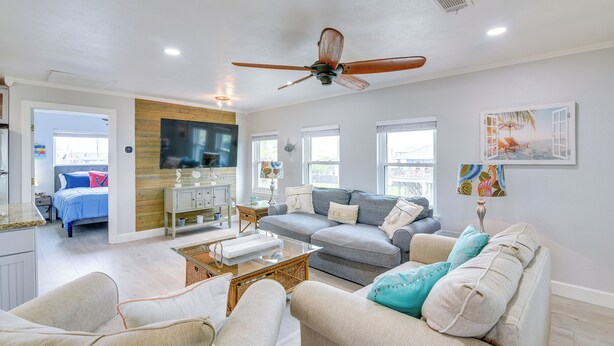 A spacious living room with a ceiling fan, a grey sofa, a coffee table, and a television. - Retreat w/ Hot Tub & Fenced Yard: Walk to Beach (Port Bolivar)