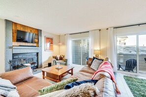 Ein gemütliches Wohnzimmer mit Kamin, bequemen Sitzgelegenheiten und einem großen Fenster mit Blick ins Freie.