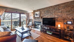 A cozy living room with a fireplace, a flat-screen TV, and a comfortable seating area with a view of the outdoors. - Galena Townhome w/ Deck & Golf Course View! (Galena)