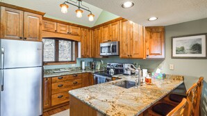A kitchen with wooden cabinets, stainless steel appliances, granite countertops, and a bar area with seating. - Galena Townhome w/ Deck & Golf Course View! (Galena)